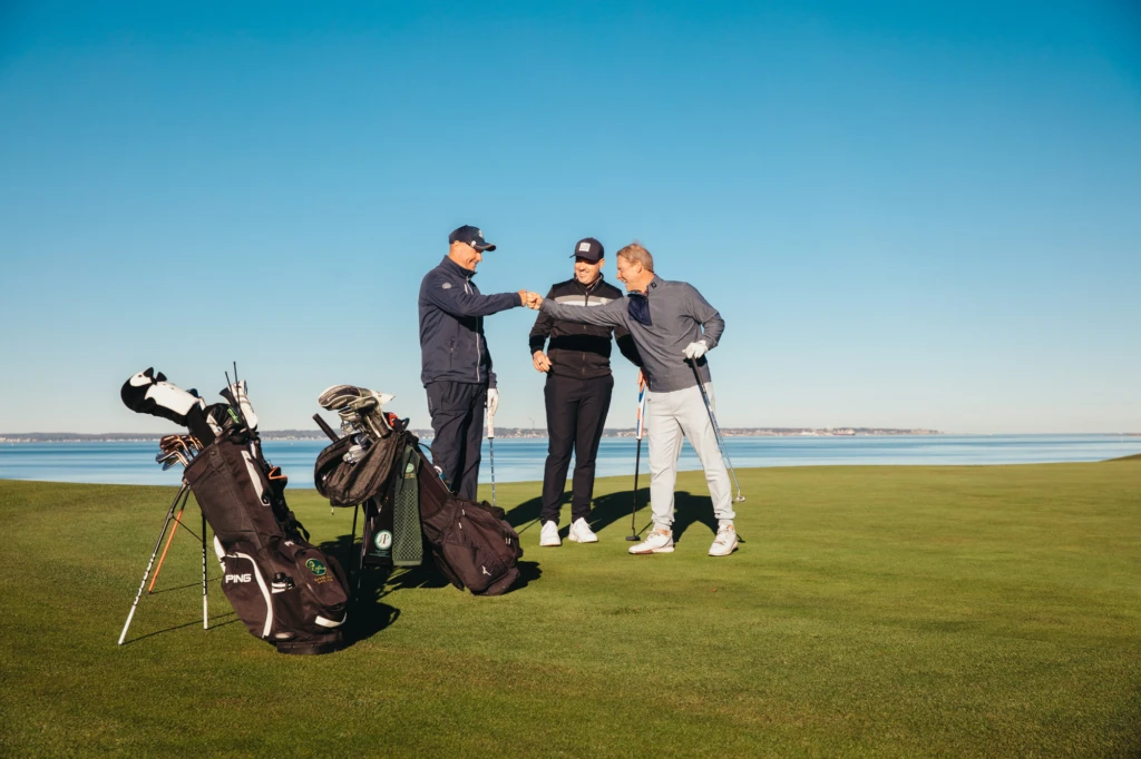 tre män på en golfbana med havet i bakgrunden